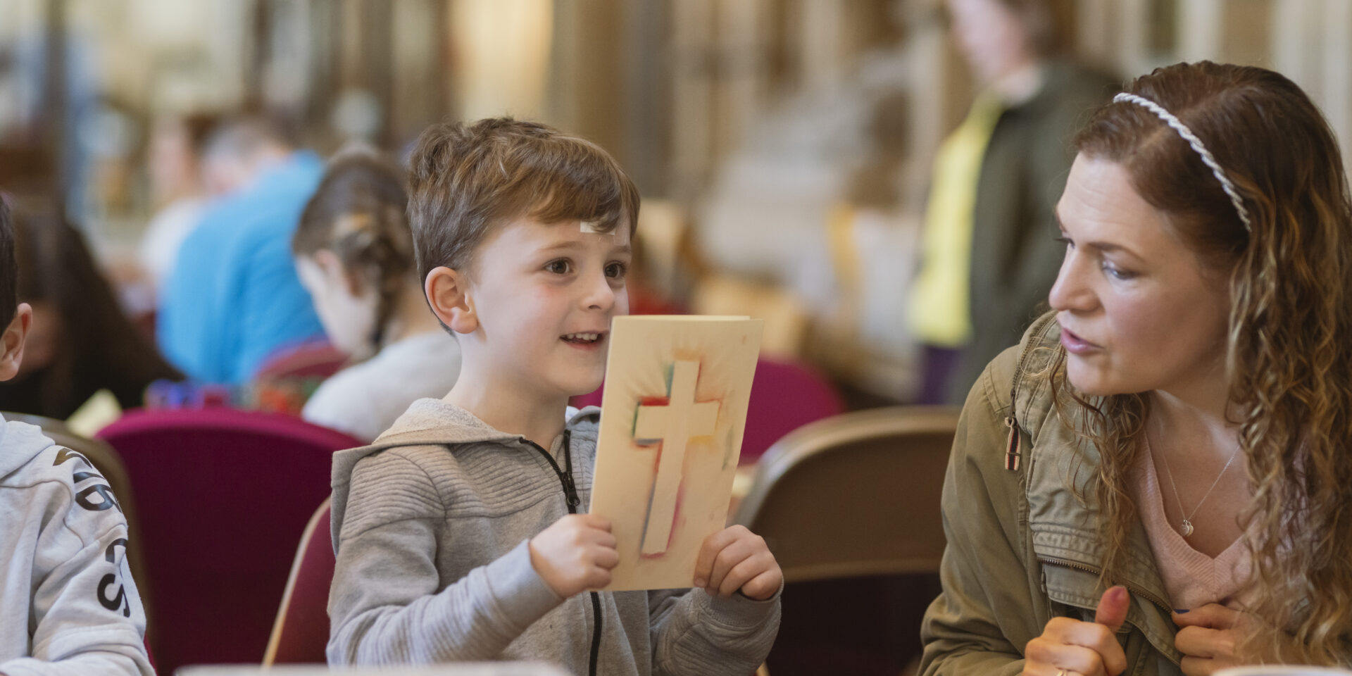 Boy proudly holding up a colourful pastel cross he made during Crafty Cathedral.
